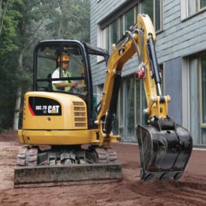 A mini excavator digger raking earth in front of a house